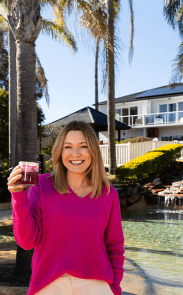 Lady in pink top holding a drink infront of hotel surrounded with palm trees