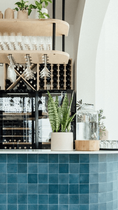 Dark blue tiled bar with martini and flute glasses hanging from an overhead glass rack