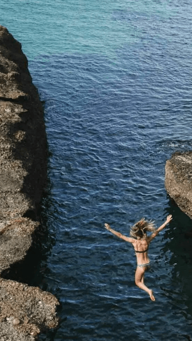 Woman jumping off the rocks into the ocean