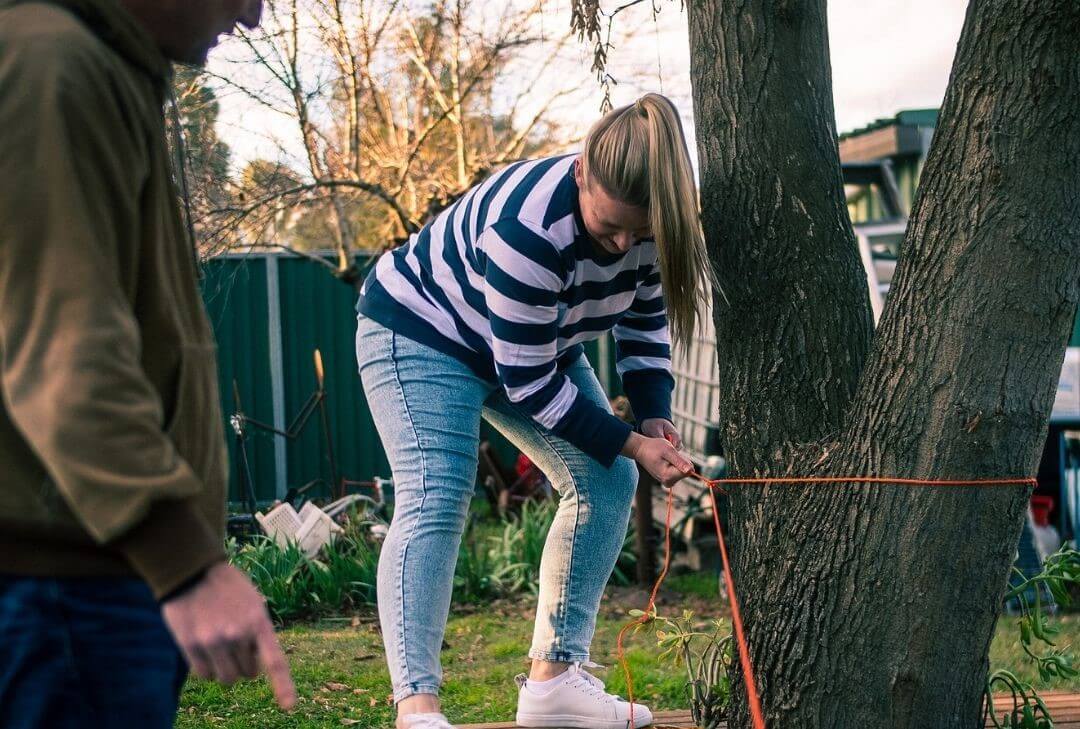 woman tethering a household backyard item to a sturdy tree