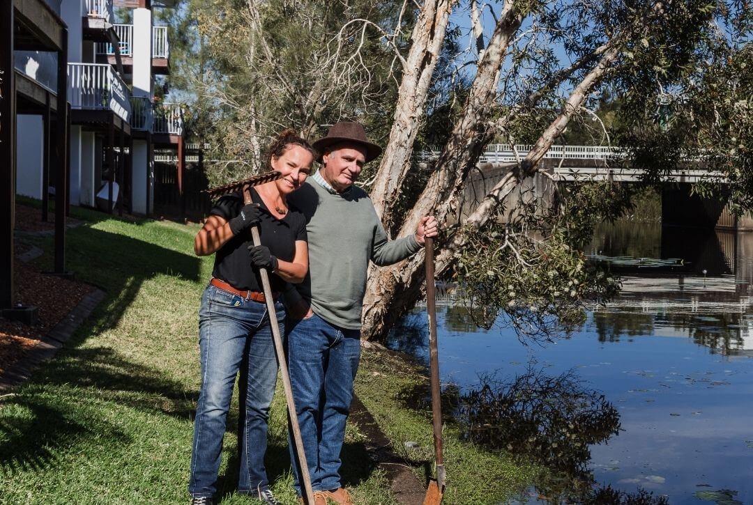 Pair of people by a low lying creek saying hello while preparing for a weather event with tools