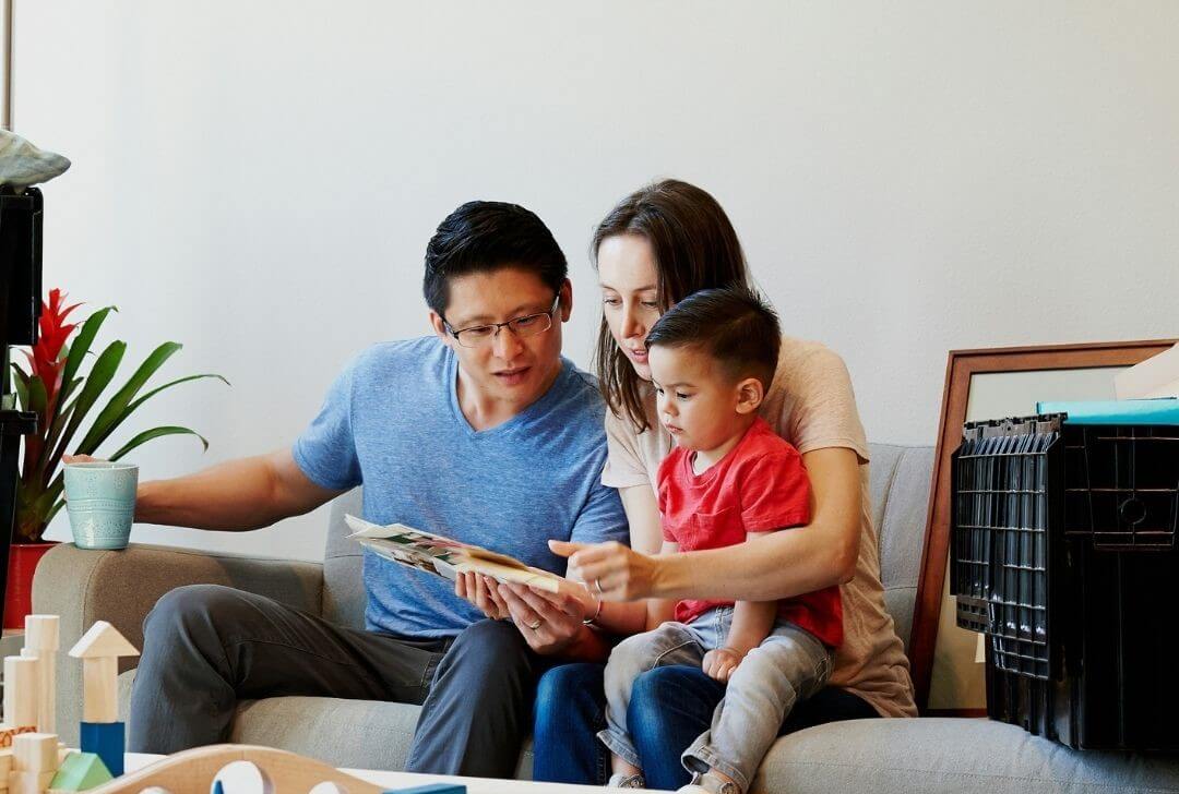 couple with young child sit around a screen planning their trip on sofa