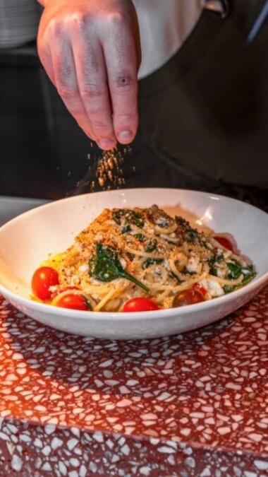 Bowl of pasta with cherry tomatoes being sprinkled with parmesan cheese from Lago Cucina in Budgewoi