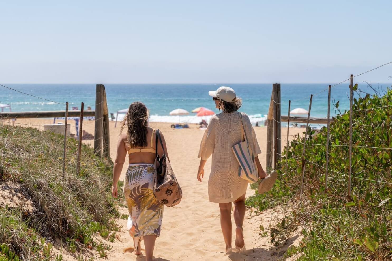 Two women walking down a sandy path towards the ocean for a day relaxing at the beach