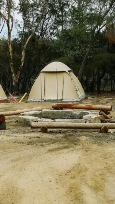 A beige canvas tent with a campfire in front ready to be lit