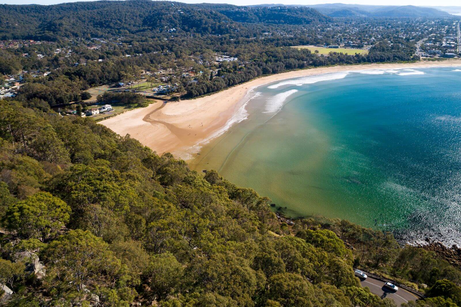 Drone shot of a beach surrounded by lush dark green bushland