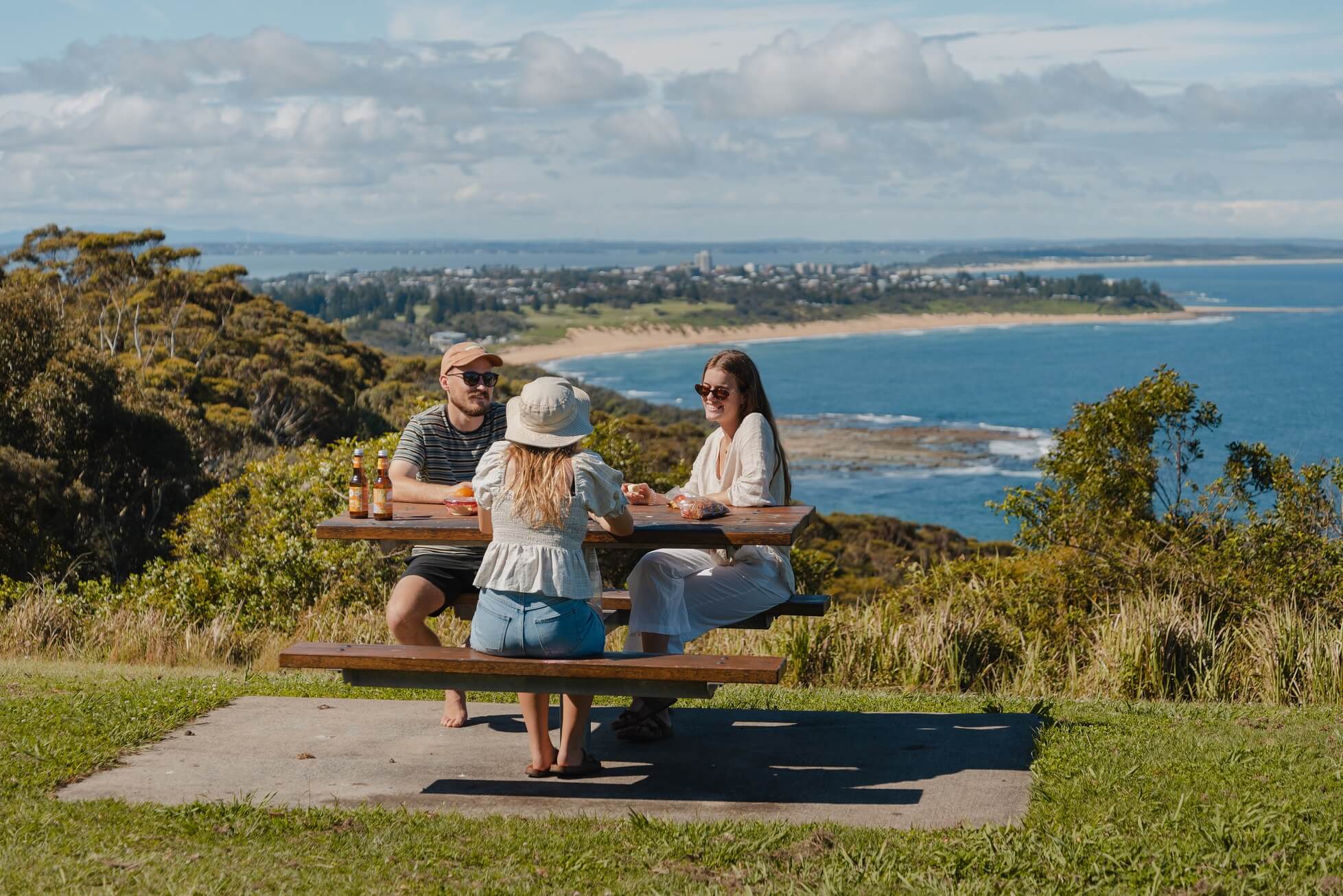 Three people sitting at a picnic table at a lookout