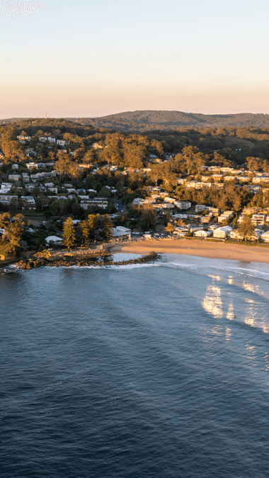 Drone image overlooking Avoca beach, cliffs and residential area at sunset