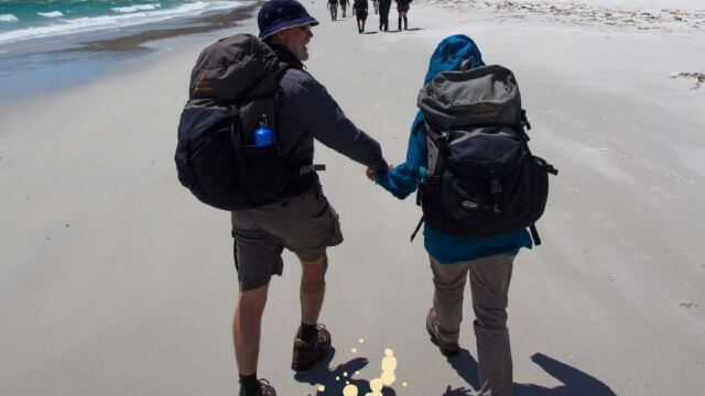 couple hiking on beach with backpacks