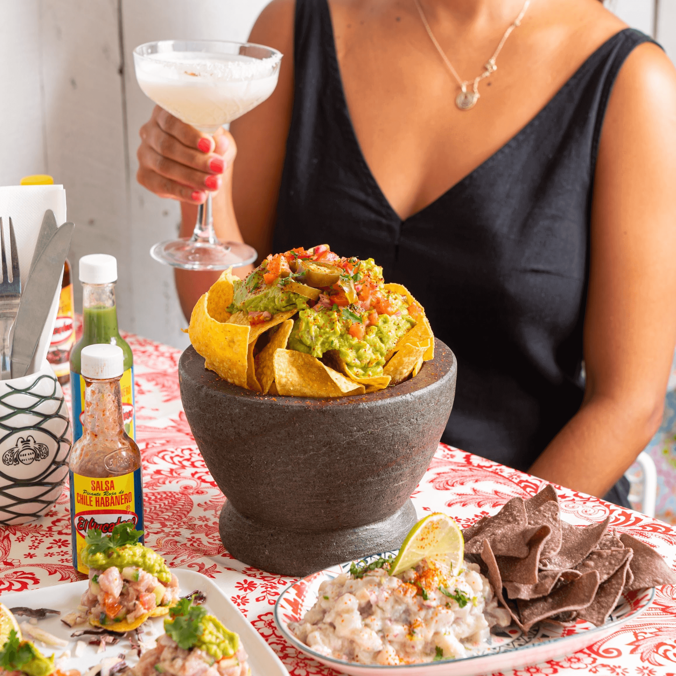 Giant bowl of loaded nachos on a table setting with other mexican food and sauces.