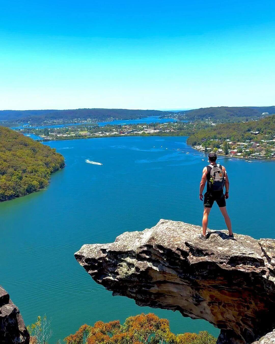 man stands proud on rocky lookout edge over bay