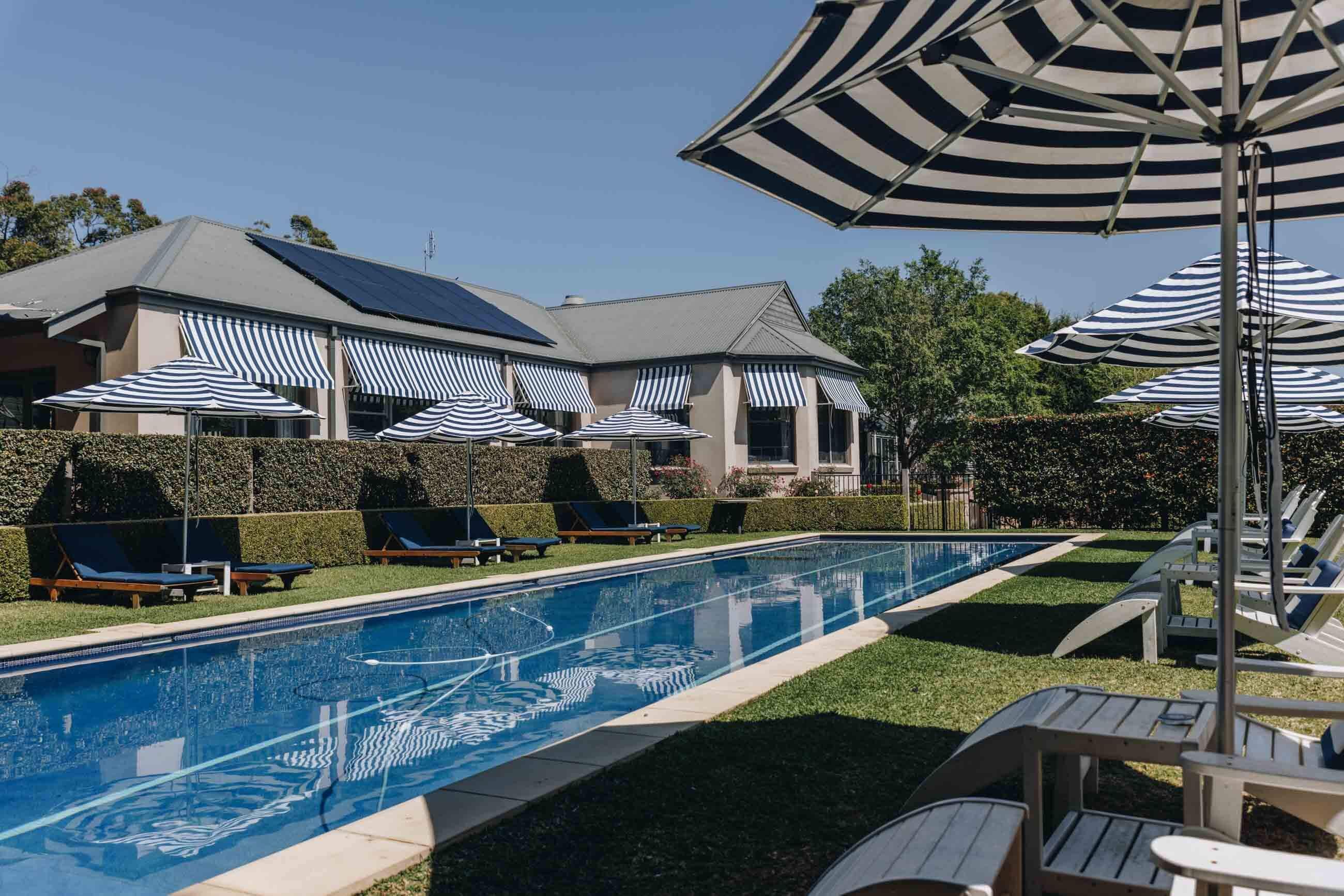 blue pool with several deck chairs and striped umbrellas surrounding with Hamptons vibe