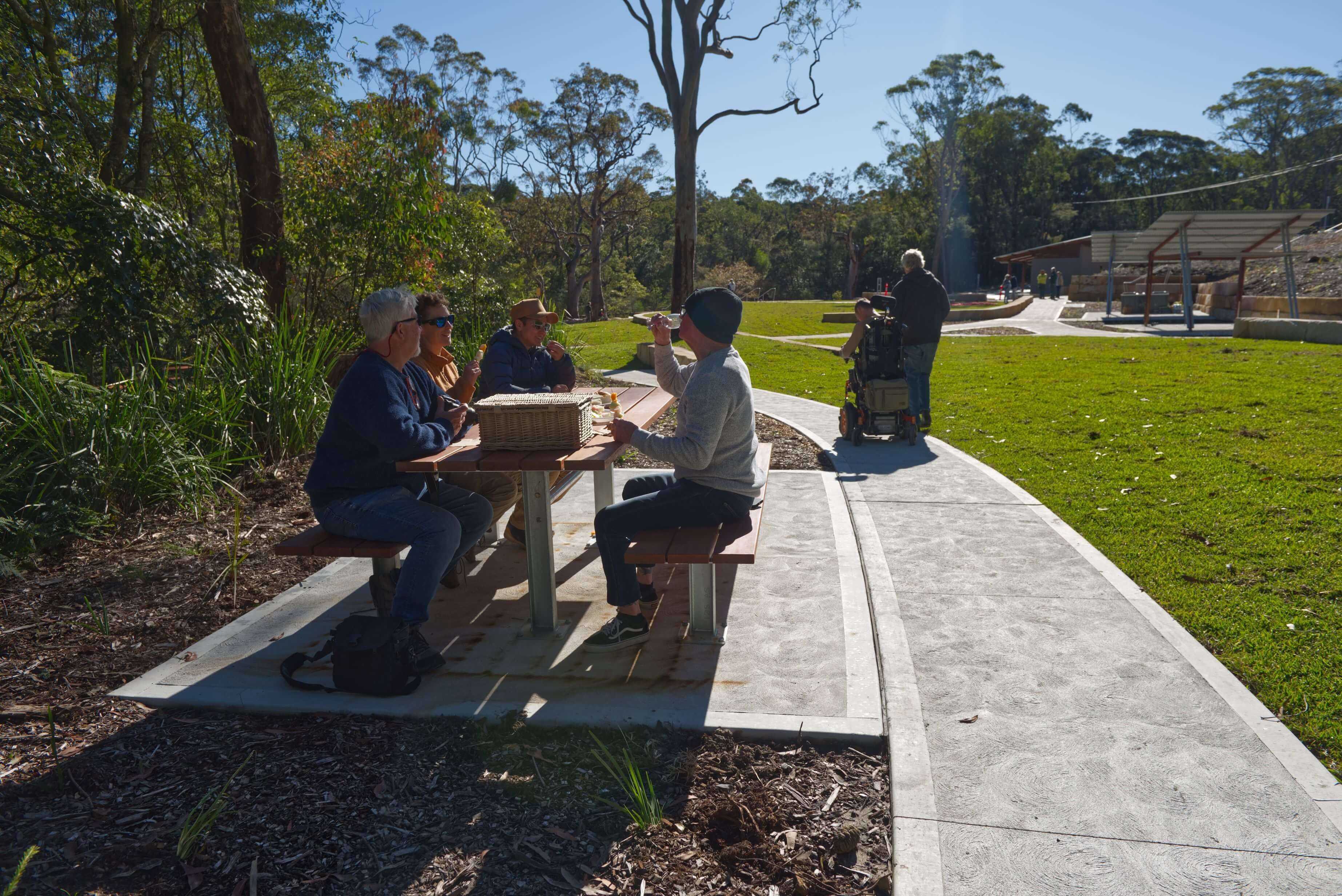 Group of people at Somersby Falls picnic table and another visitor passing by using a wheelchair access path