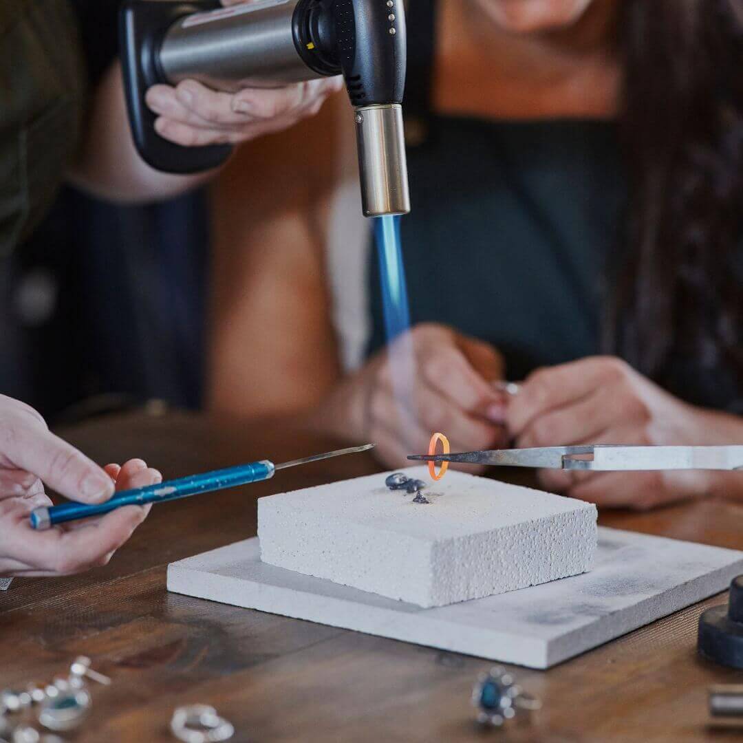 A focused woman applies a torch to heat jewelry, demonstrating her skill and dedication to the art of jewellery making.