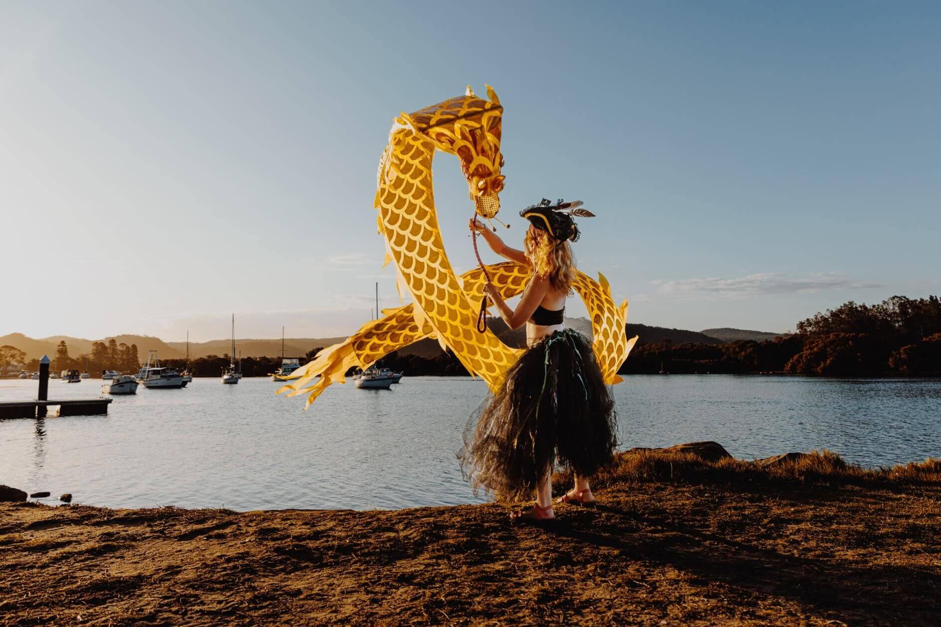 Dancer with dragon standing near water at sunset