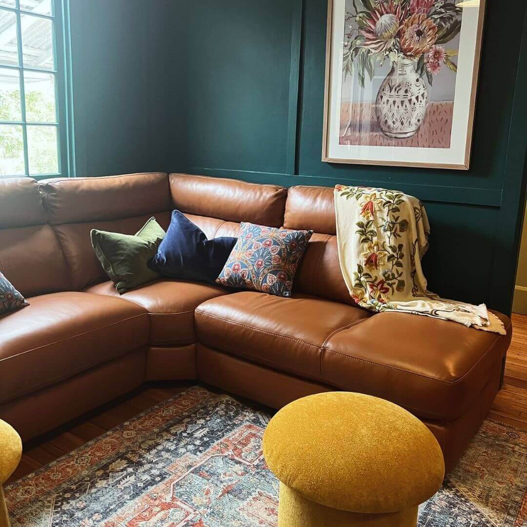 A stylish leather sectional sofa paired with vibrant yellow ottomans, set against a refreshing green wall backdrop.