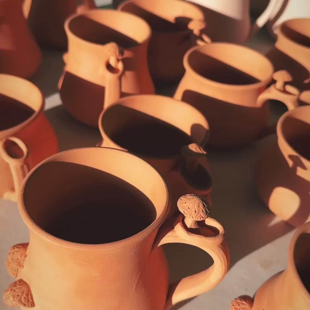 A small collection of freshly fired terracotta-coloured mugs ready to be glazed.