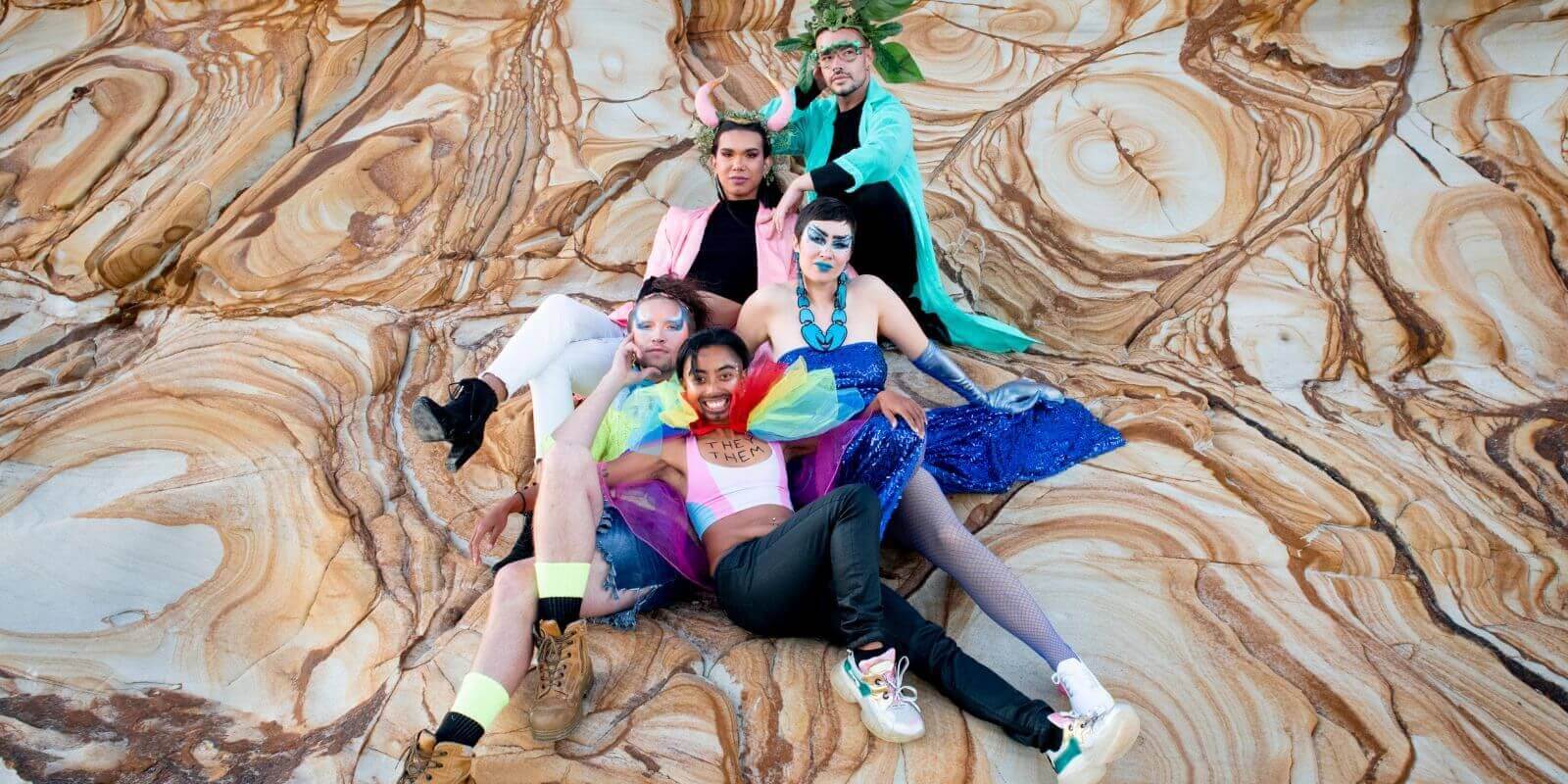 Five people sitting on rocks at the beach wearing colourful clothing