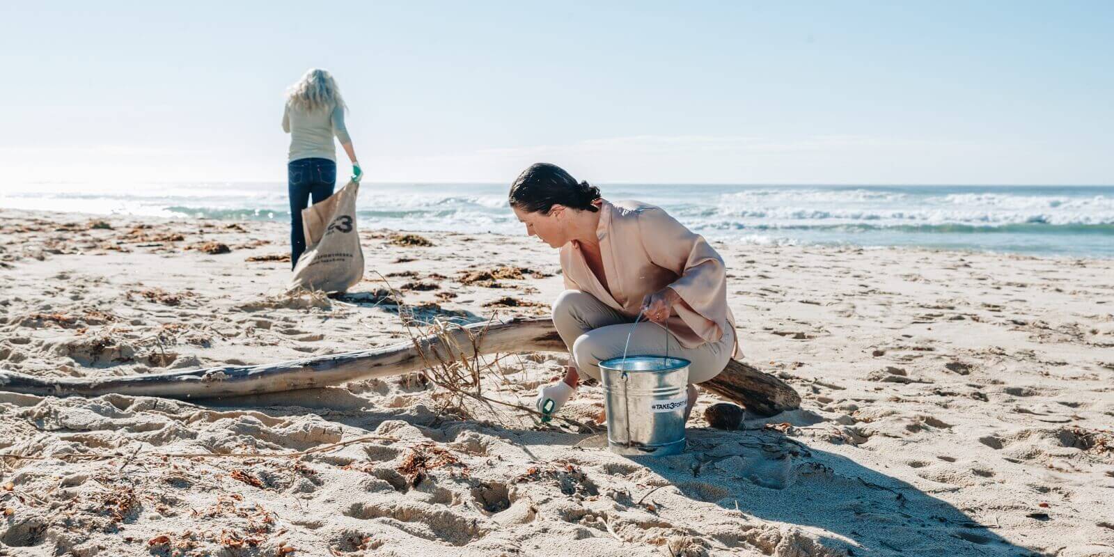 Two women picking up pieces of rubbish on the sand at a beach