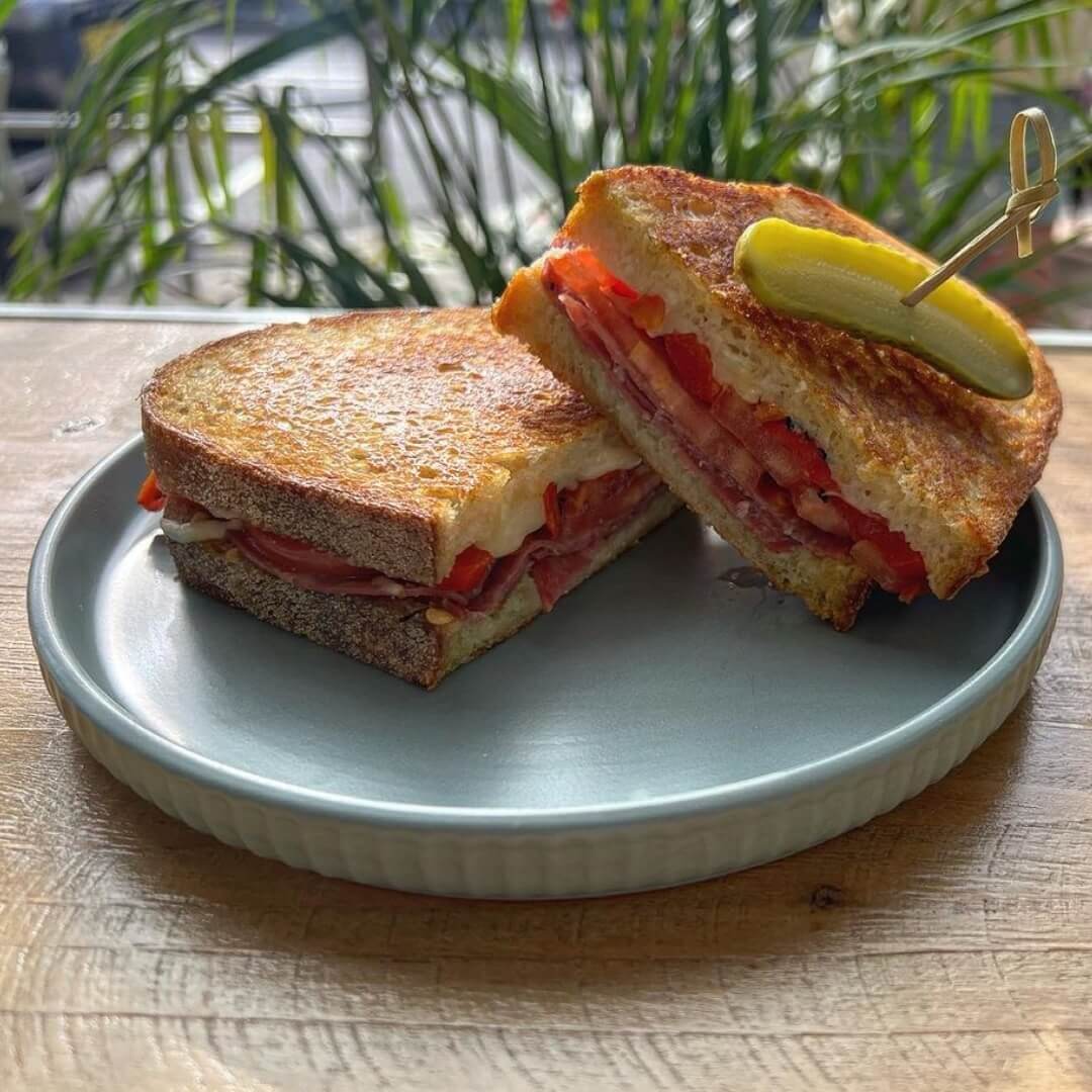 A freshly toasted salami, tomato and roasted capsicum sandwich, with a sweet tangy pickled skewered into the top of the sandwich.