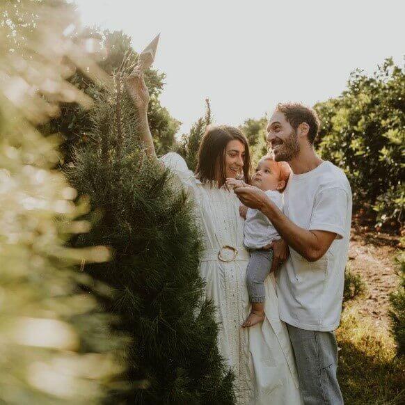 A couple and a baby putting a star on top of a real pine Christmas tree in a pine tree field