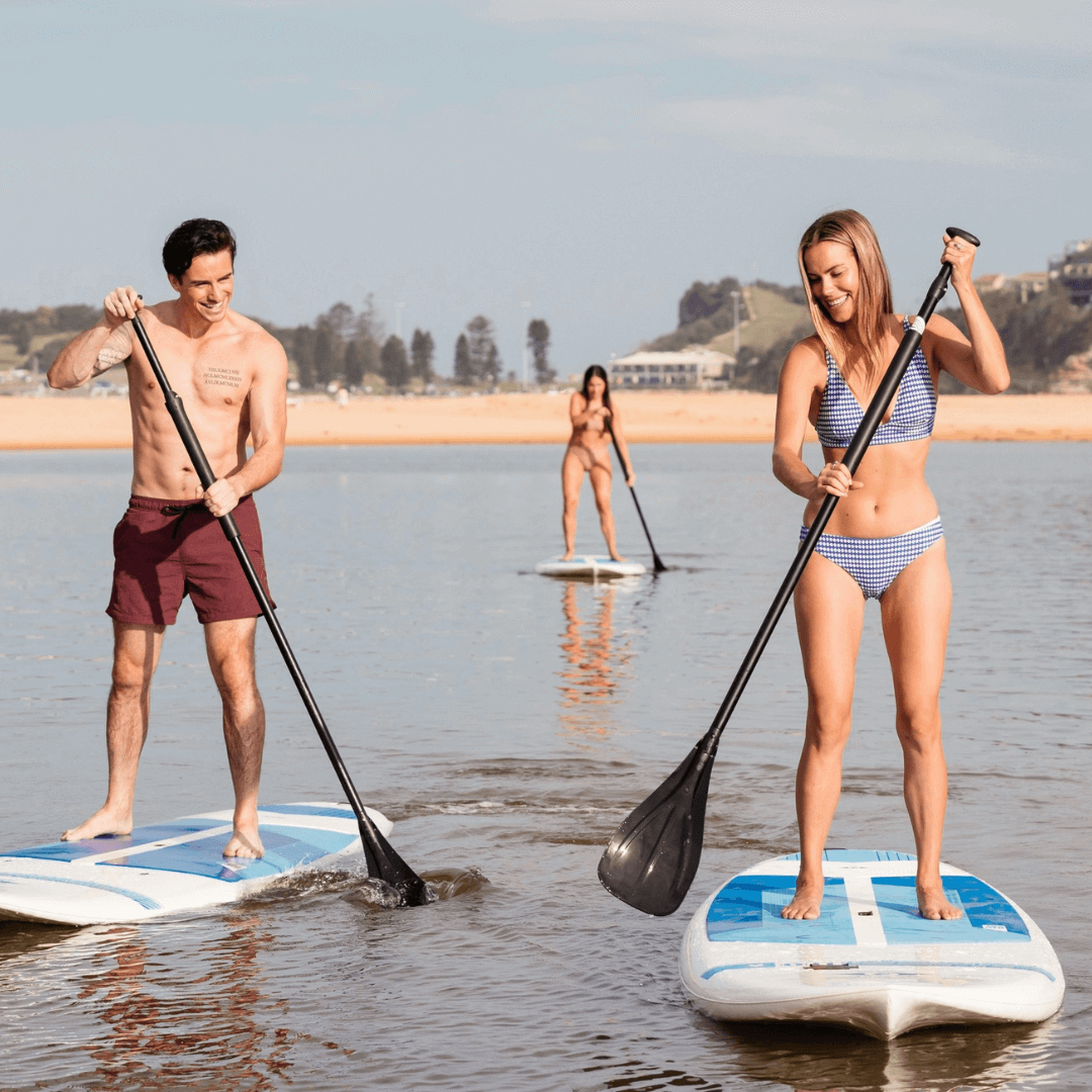 A man and woman stand up paddleboarding across a calm lake. A lady is also paddleboarding in the background