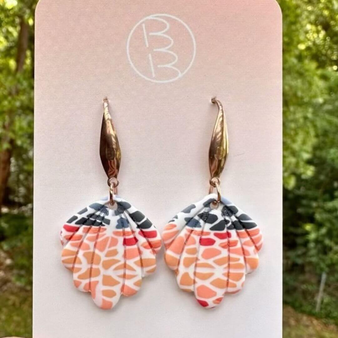 A set of seashell-shaped dangle earrings. The earrings are a mix of peach-coloured blobs and blue-grey coloured blobs on a white background.