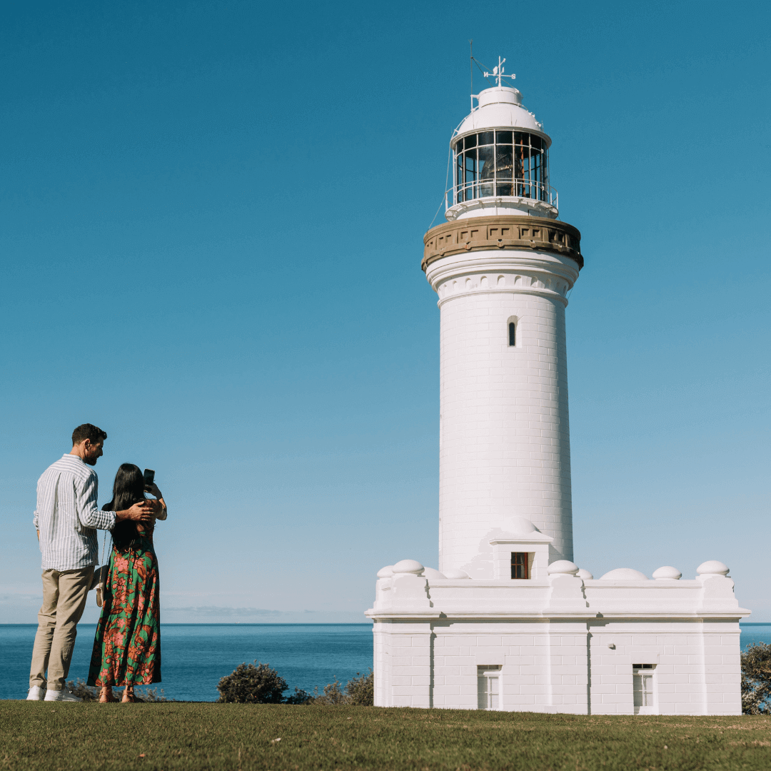 A couple taking a photo of a tall, white lighthouse