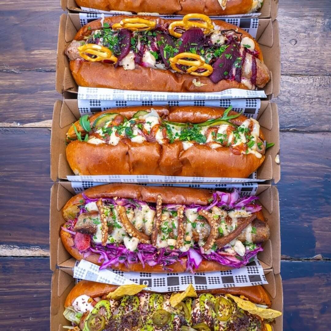 Four fresh hotdogs placed in a cardboard container, lined up in a row filled with svaoury fillings.