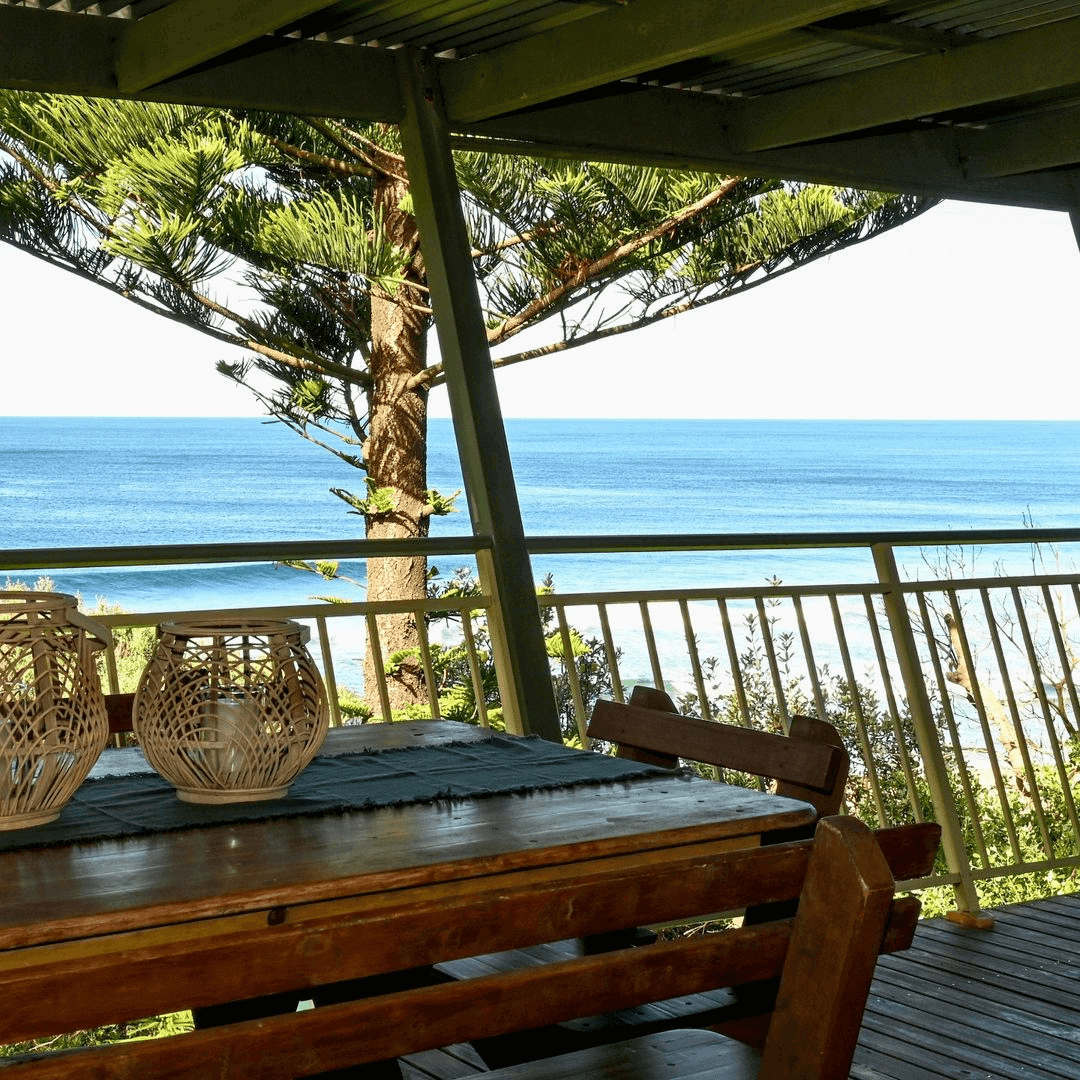 A holiday cabin deck with a view of the ocean. On the deck sits an outdoor wooden table.