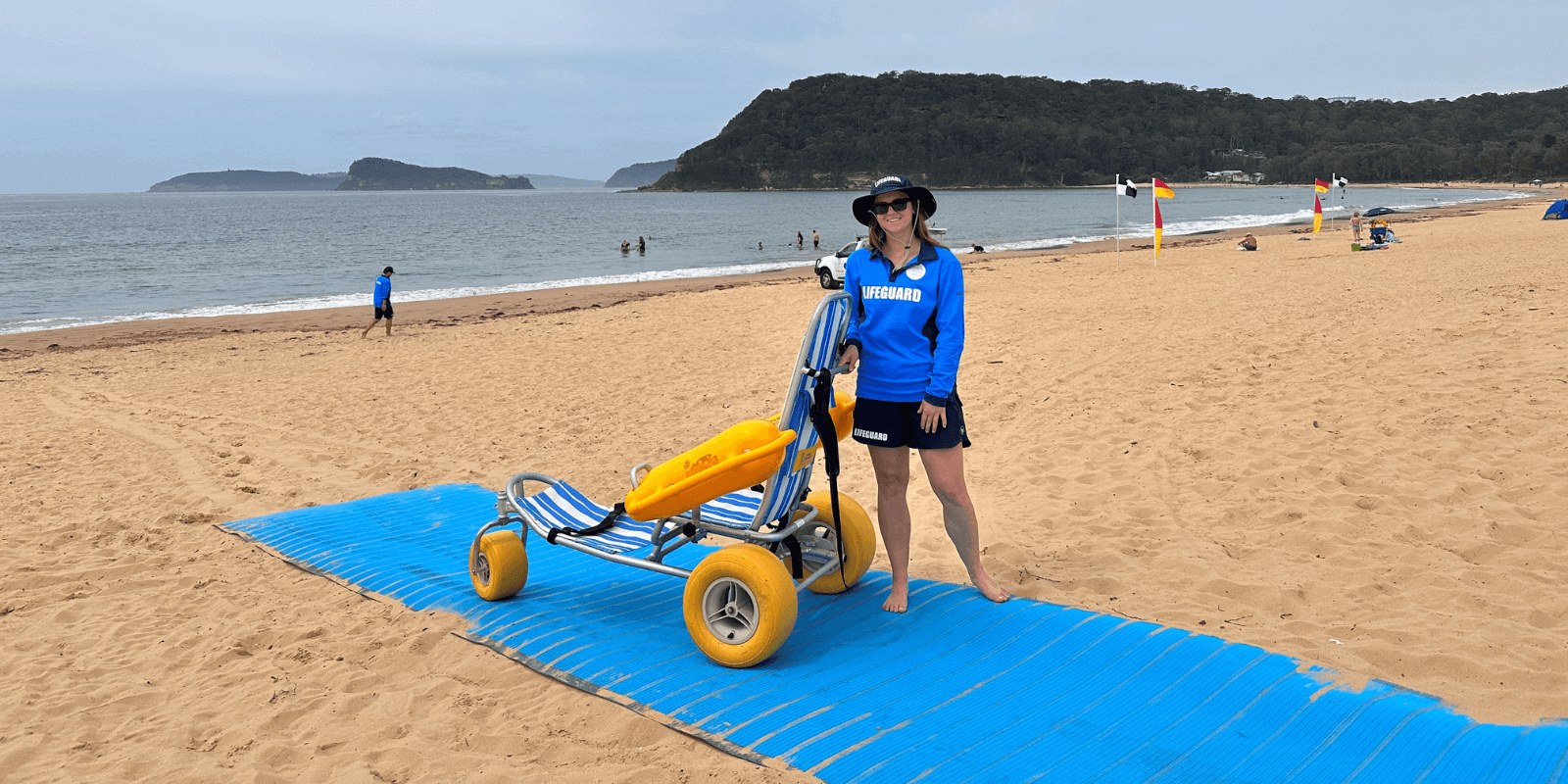 accessible beach buggy on beach mat and lifeguard wearing blue and white uniform