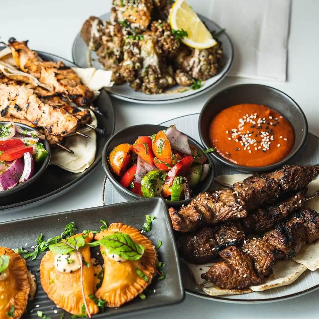 Various plates of Middle Eastern tapas including kebabs, curry puffs and dips