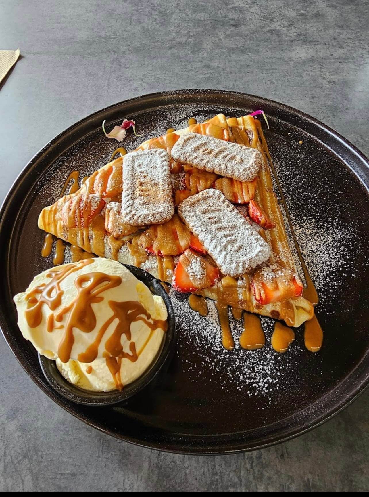 A plate of crepes adorned with Lotus biscoff spread and biscuits, and a scoop of vanilla icecream on the side