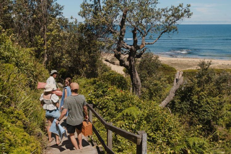 A group of people walking down wooden stairs to a beachfront.