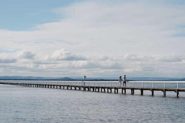 A man and woman walking along a long jetty that juts out into the middle of a lake