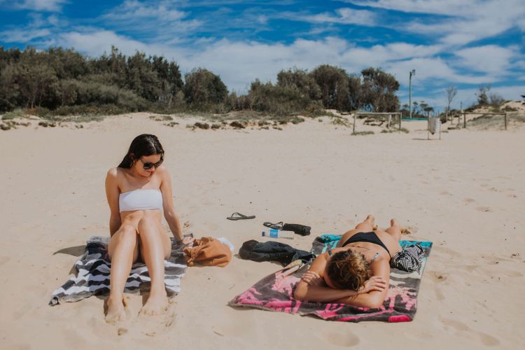 Two women wearing bikinis sunbaking on the sand of Umina Beach