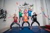 Two circus instructors and their youth students in a human pyramid holding Juggling clubs and ribbons in a circus studio. Background wall says roundabout circus. 