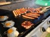 Bacon, eggs and sausages cooking on a barbecue